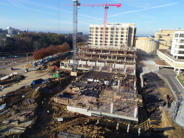 Aerial view of a construction site with a multi-story parking deck under development by Vondace Contracting, featuring scaffolding, a crane, and construction materials, adjacent to a roadway.
