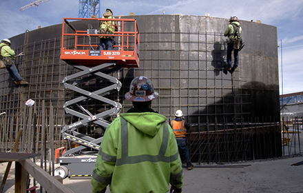 Construction workers installing rebar on a concrete structure with the assistance of an aerial lift, emphasizing safety metrics.