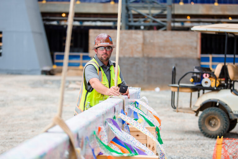Construction worker in high visibility vest resting on a barrier at a construction site.