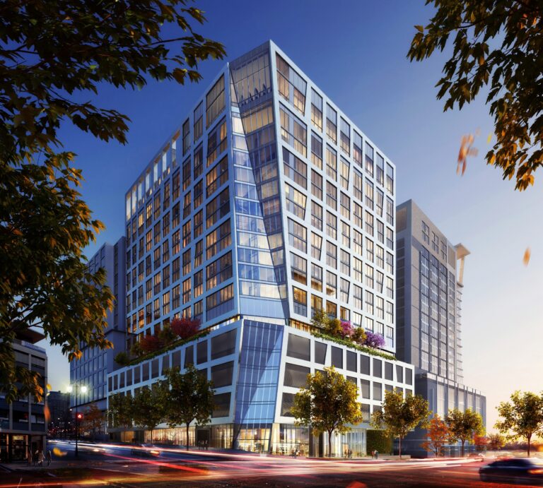 Modern glass-clad building at dusk with illuminated windows and bustling street activity.