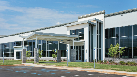 Modern commercial building with large windows and a parking lot on a sunny day.