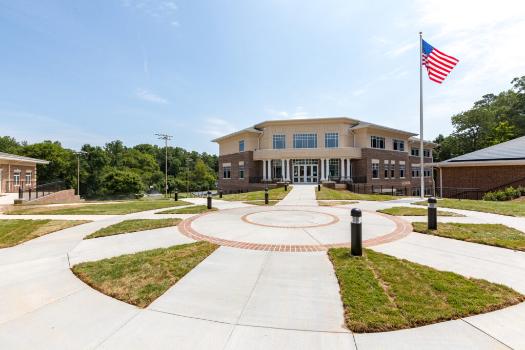 A modern educational building, a Vondace Contracting Project, with an American flag fluttering in the front courtyard under a clear blue sky.