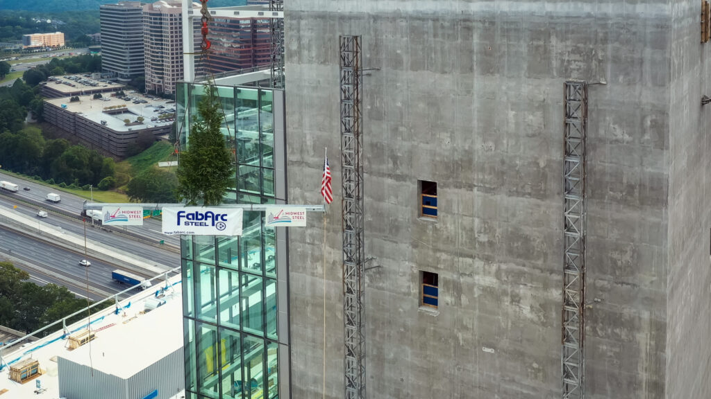Construction site with a TK Elevator test tower nearing the topping-out milestone next to a highway.