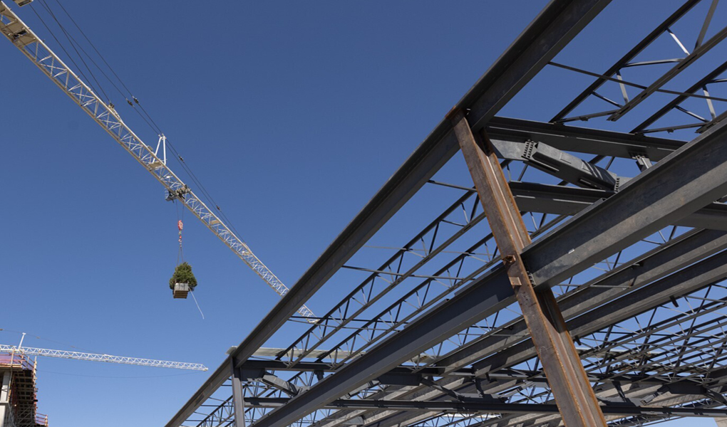 Crane hoisting materials above the Vondace Contracting's steel framework at a construction site against a clear blue sky.
