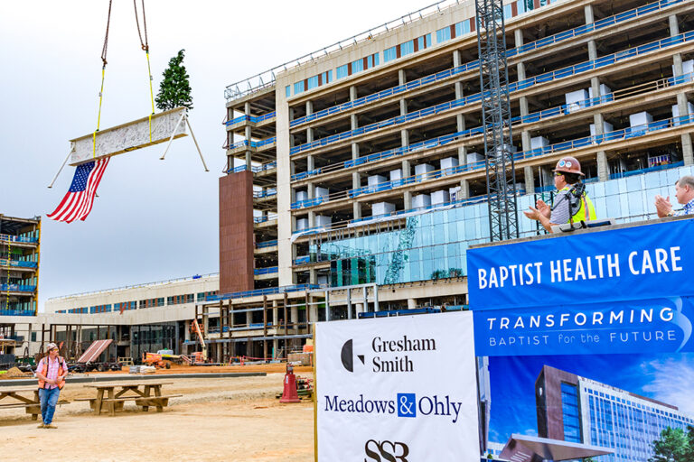 Construction workers observing as a large American flag is hoisted at a building site with a crane during the Topping Out ceremony organized by Vondace Contracting for the Baptist Health Care project.