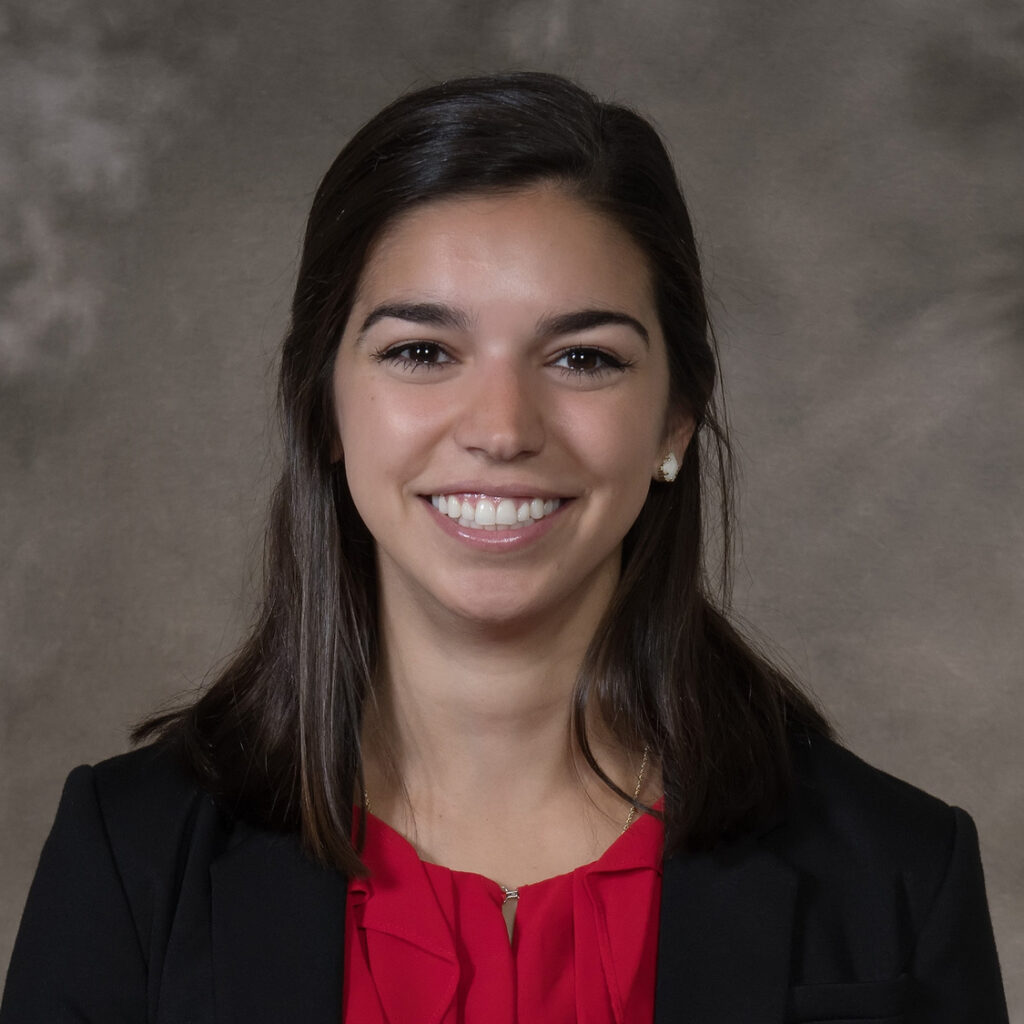 Professional portrait of a smiling woman with dark hair, wearing a red blouse and black blazer, celebrating Women in Construction Week.