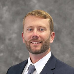 Portrait of a smiling man with a beard wearing a suit and tie against a gray background, recognized as a Miami leader in ENR Southeast for his influence on construction trends.