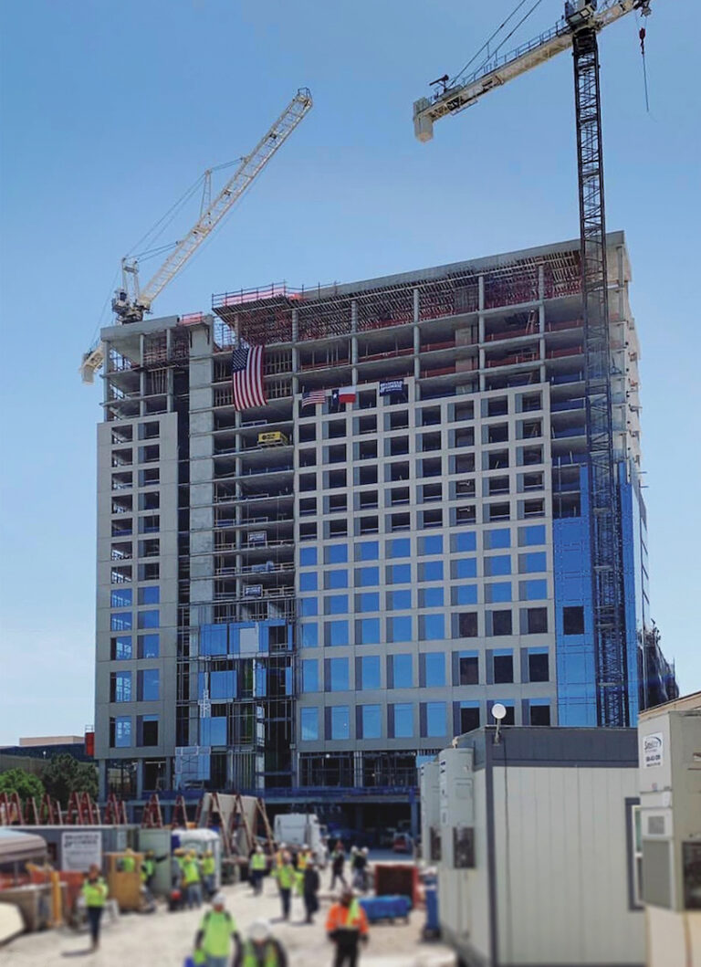 Construction workers in safety vests at a Vondace Contracting building site with cranes and a partially completed high-rise commercial real estate market project displaying an American flag.