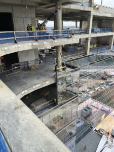 Construction workers engaged in high-rise building construction with multiple large floors visible and the use of safety harnesses and scaffolding.