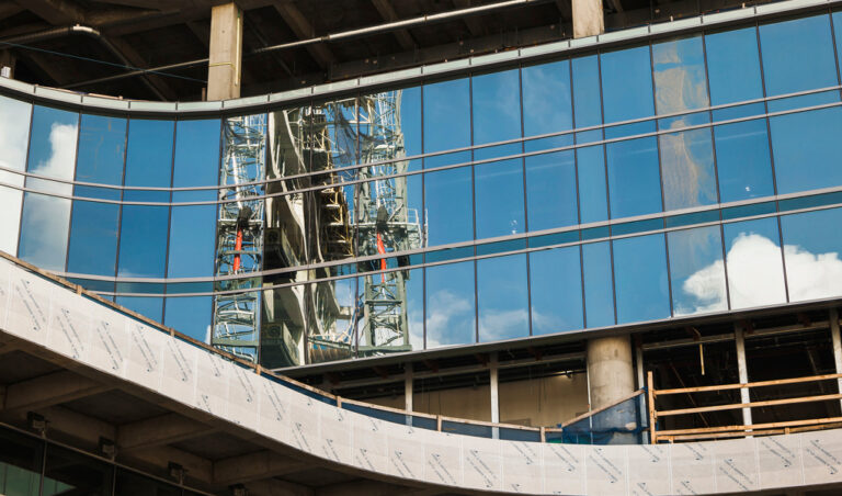 Reflection of a large construction crane on the glass facade of a building under construction.