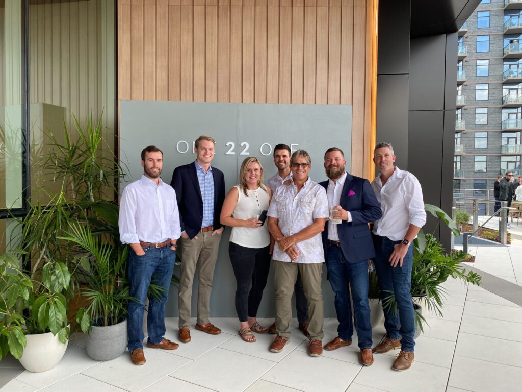 Group of seven individuals posing for a photo in front of a sign that reads "ONE22ONE" on an outdoor terrace at Nashville's Gulch.