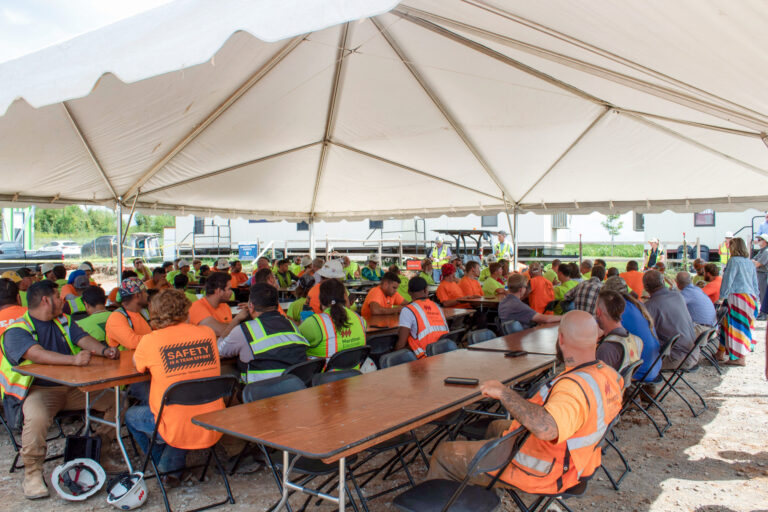 Workers in high-visibility vests attending a Tops Out meeting for the Vondace Contracting Life Sciences Facility under a large tent.