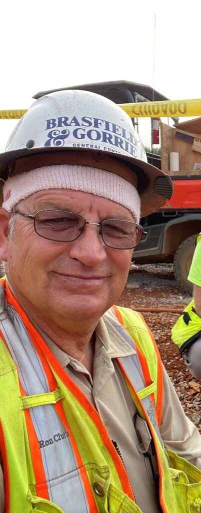 A construction worker wearing a hard hat and high-visibility vest takes a selfie at a construction site.