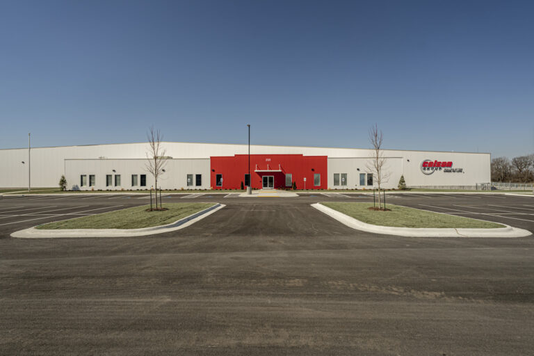 Modern industrial warehouse with red entrance and empty parking lot, serving as a Vondace Contracting Manufacturing Facility in Arkansas.