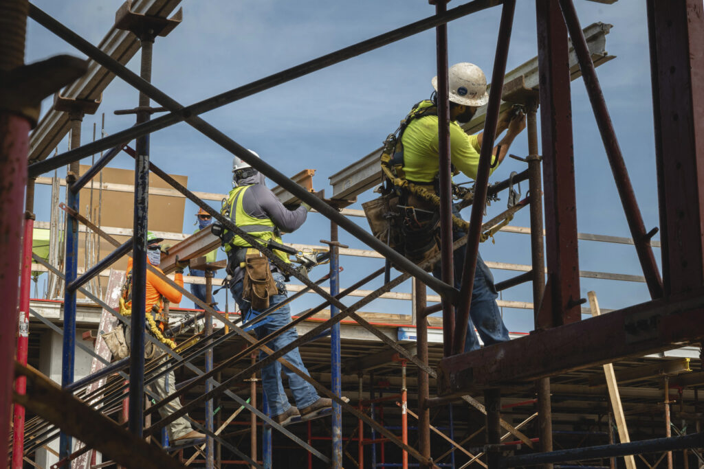 Construction workers on scaffolding with safety gear manage risk.