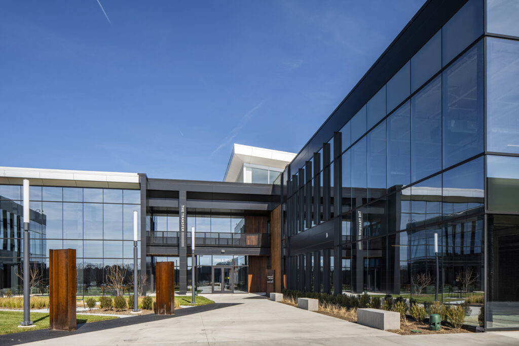 Modern office building, converted by developers from a previous structure, with expansive glass facade and landscaped courtyard under clear blue sky.