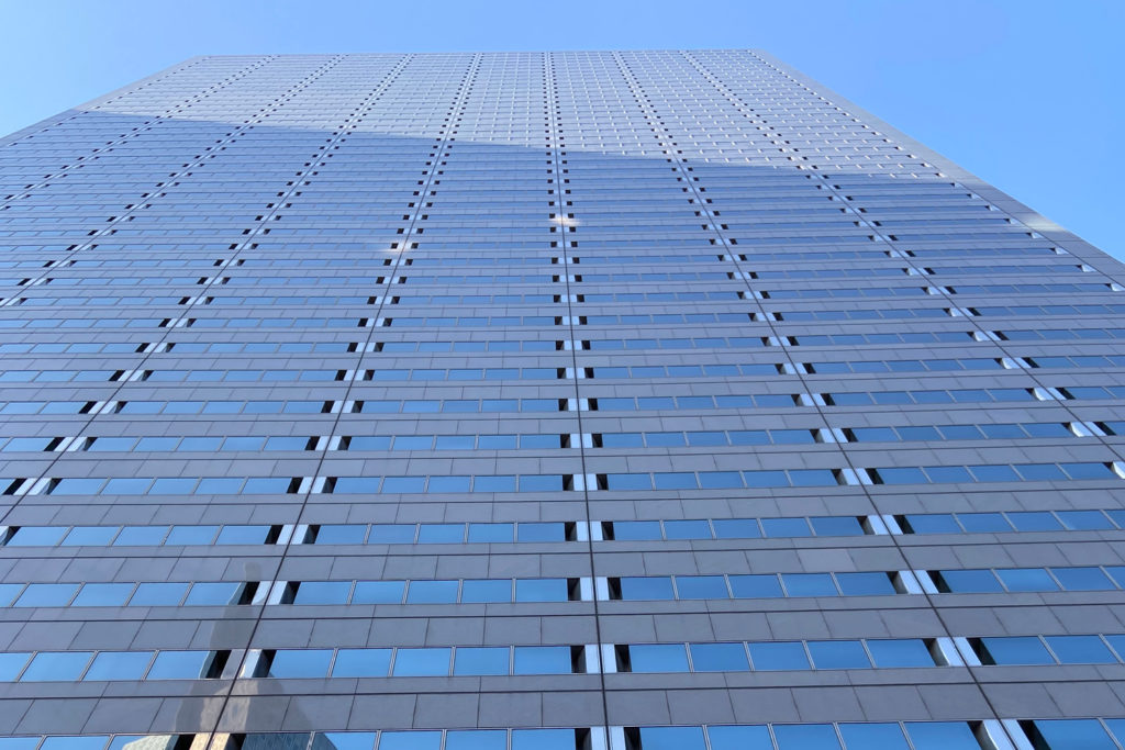 Looking up at the facade of a modern glass skyscraper, converted by developers into unique spaces, against a clear blue sky.