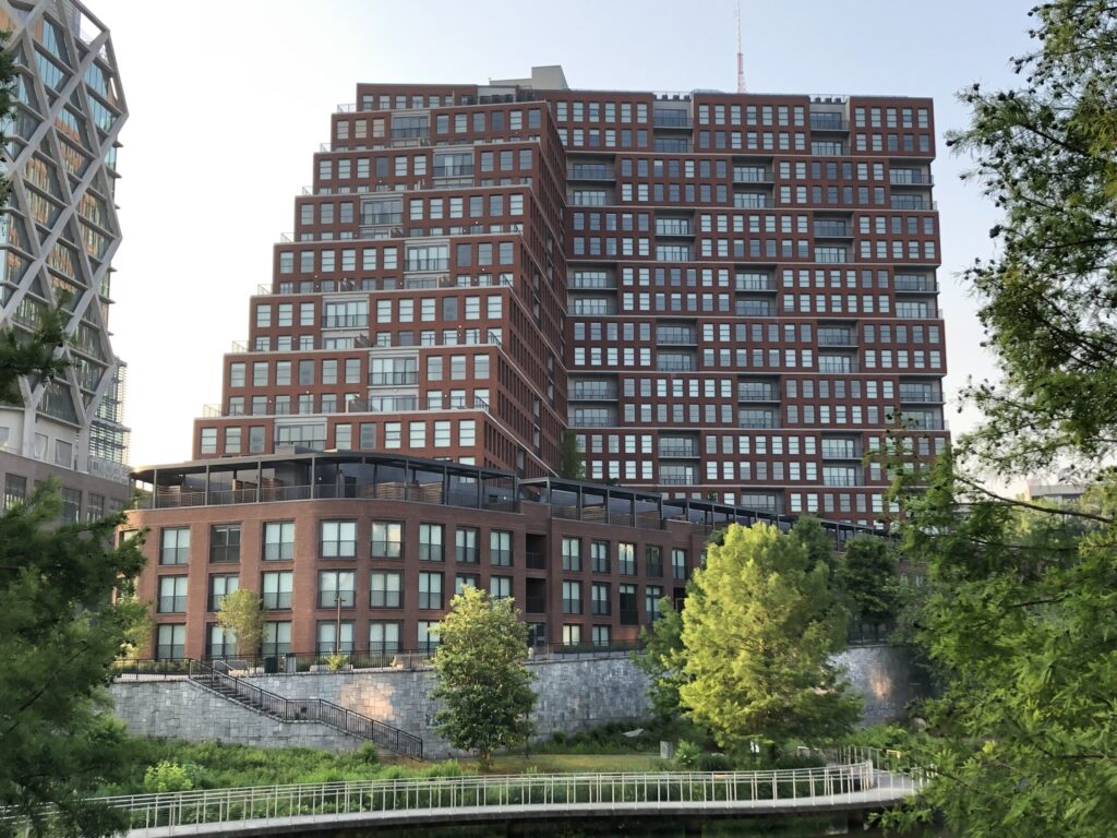 A complete modern multi-story residential tower with a brick facade, surrounded by greenery and a clear sky in the Fourth Ward Development.
