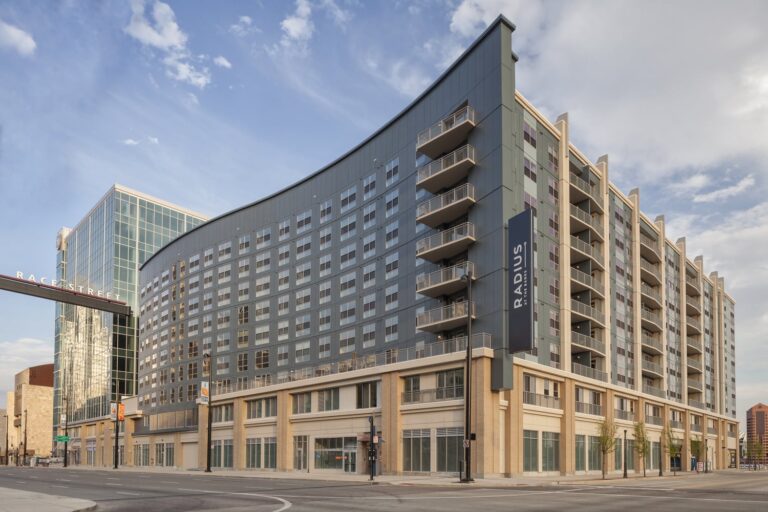 Modern multi-story multifamily housing with mixed materials and a curved facade, located at the corner of a city street.