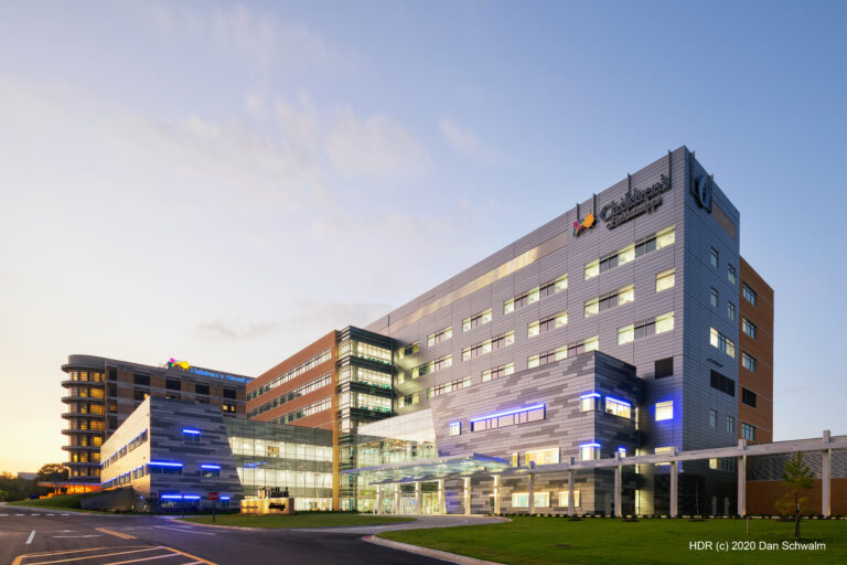 Modern hospital building with multiple stories, large glass windows, and illuminated exterior lights at dusk; signs display “Children’s of Mississippi
