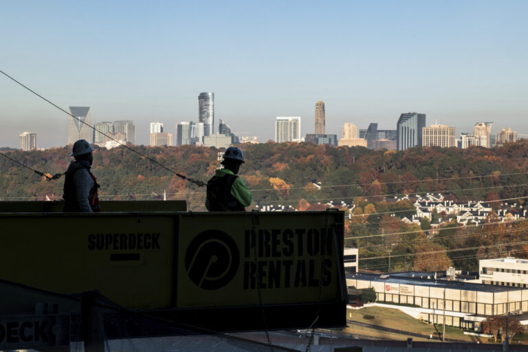 Two construction workers overlooking a city skyline from an elevated platform.