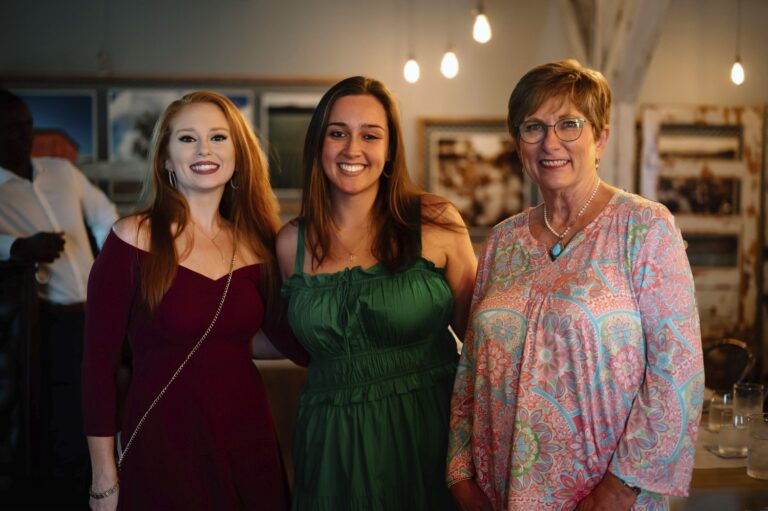 Three women posing for a photo in a room with pictures on the wall.