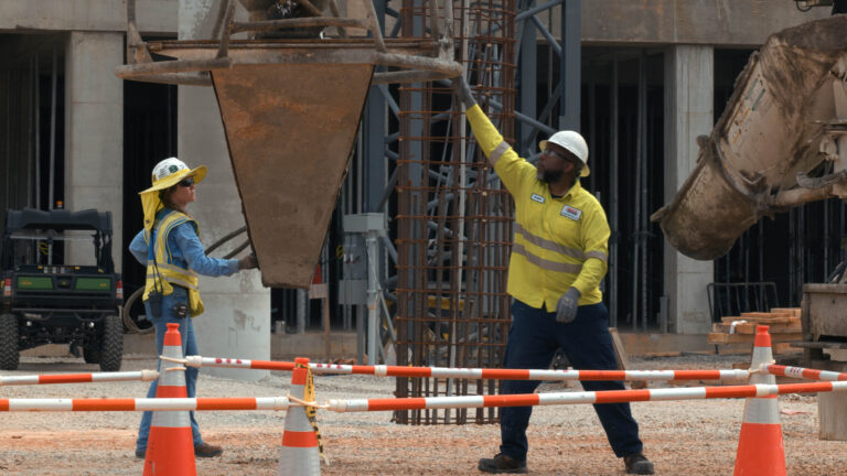 Construction workers coordinating the movement of a concrete bucket at a construction site.