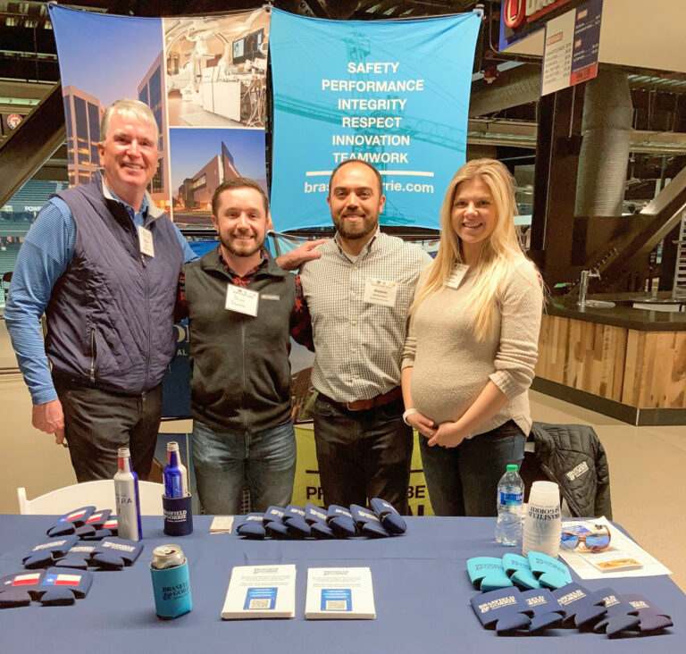 Four individuals posing for a photo behind a promotional booth with branded merchandise on display in Dallas, Texas.
