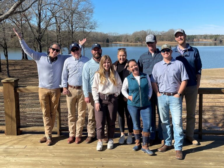 Group of people smiling on a wooden deck with a lake in the background on a sunny day, showcasing tourism in Jackson, Mississippi.