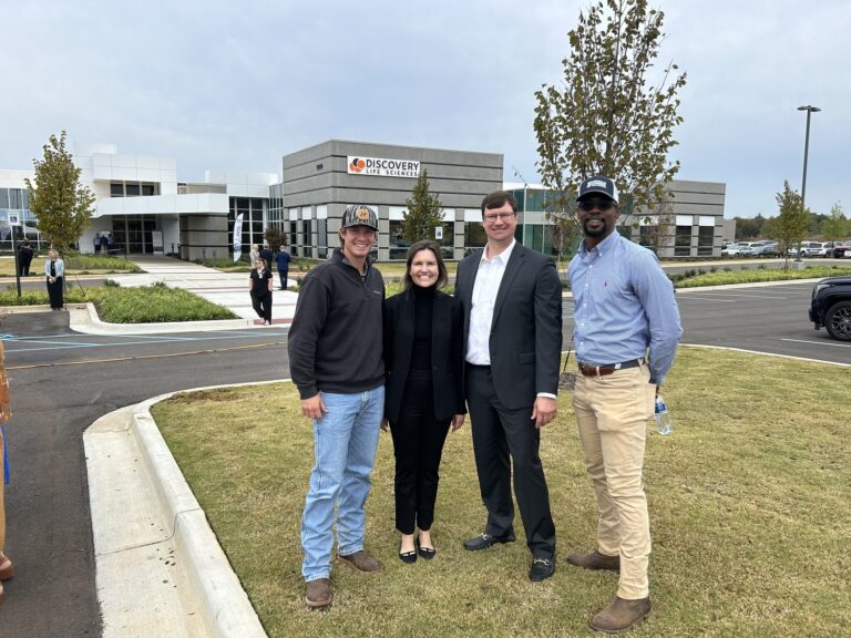 Four individuals posing together in front of a building with a 