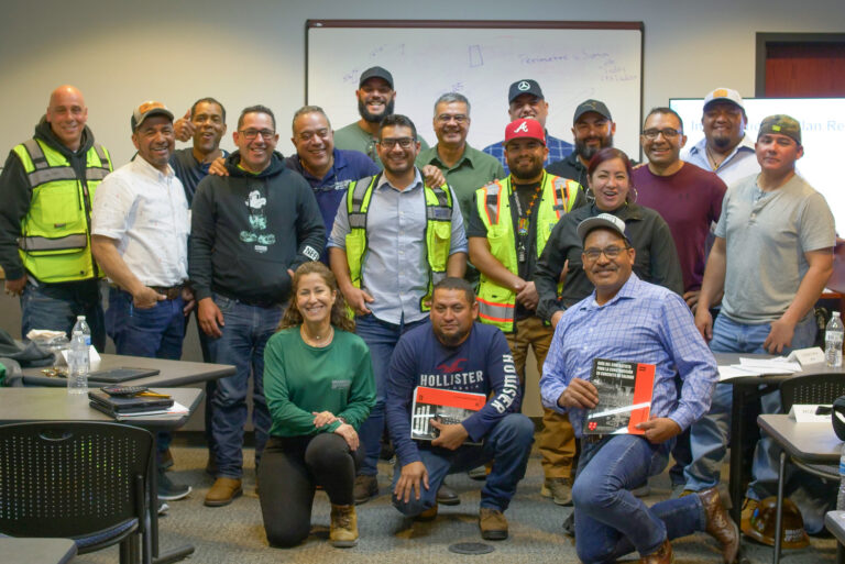 Group of workers in an Orlando, Florida classroom setting, some wearing safety vests, posing for a photo with a mix of standing and seated individuals.