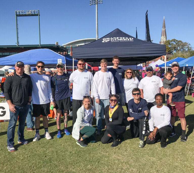 Group of people posing together at an outdoor event with tents and banners in the background.