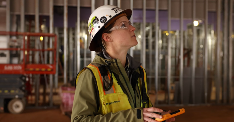 Construction worker with safety helmet holding a walkie-talkie at a skilled trades construction site during twilight.