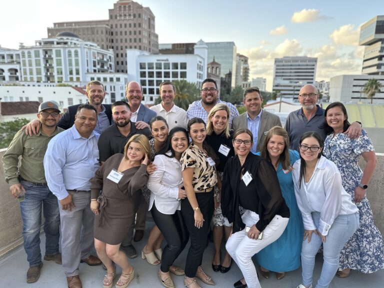 Group of professionals posing for a photo on a rooftop with city buildings in the background.