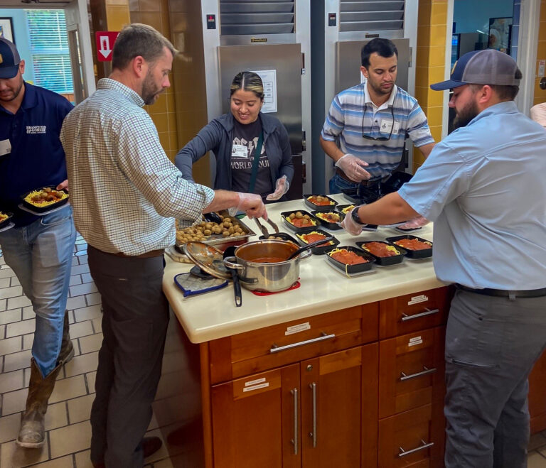 A group of people serving themselves food from a buffet-style setup in a kitchen.