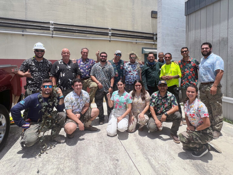 A group of people in matching floral shirts posing for a photo outdoors with a fire truck in the background.