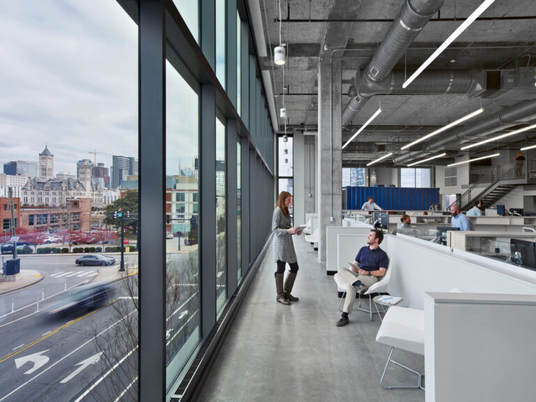 Office employees engaging in a casual conversation by the window with a city view.