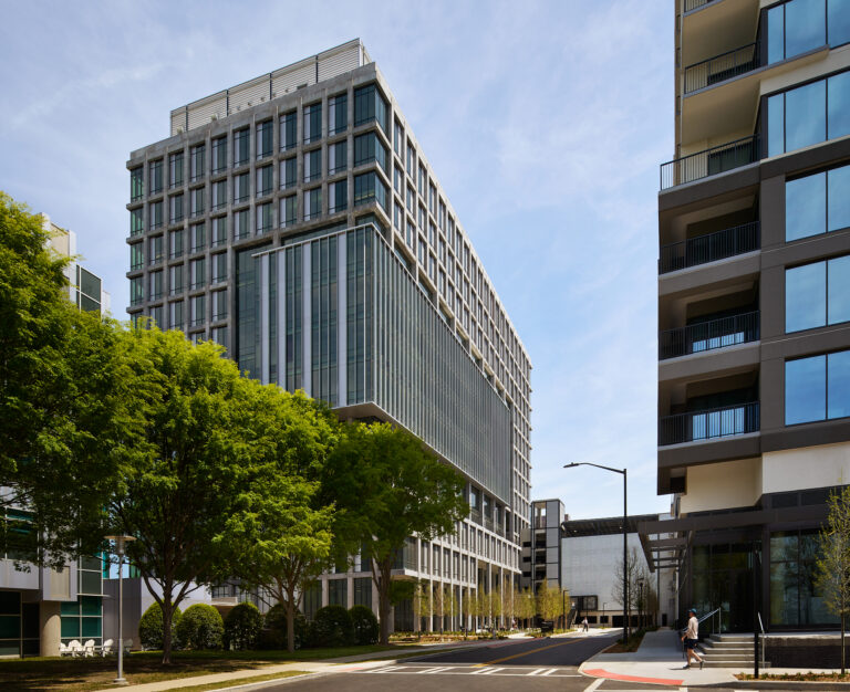 Modern office buildings with glass facades grace Science Square, nestled next to a tree-lined street under a clear blue sky.