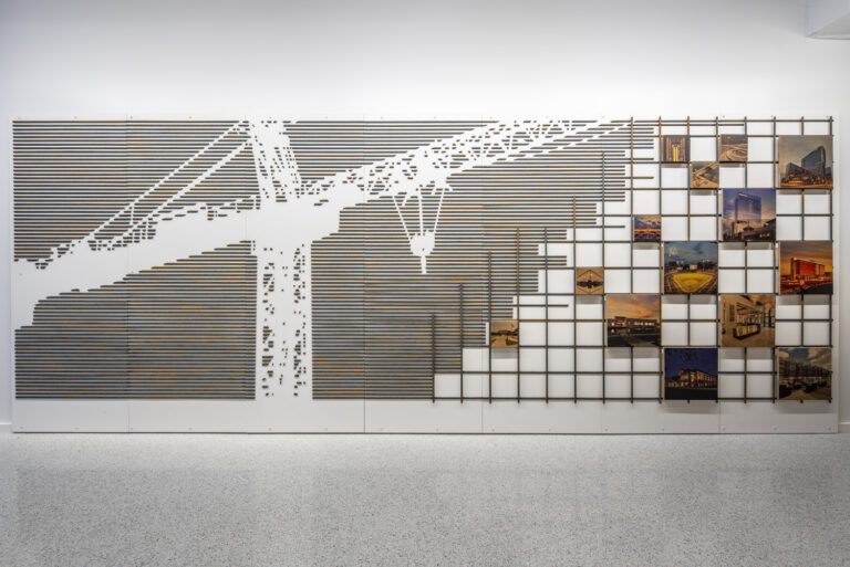 Art installation featuring a grid of black lines interrupted by photographs, with a pattern suggesting fragmentation or dispersal.