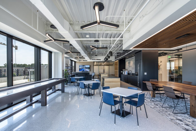 Modern office break room with a variety of seating options and large windows allowing natural light.