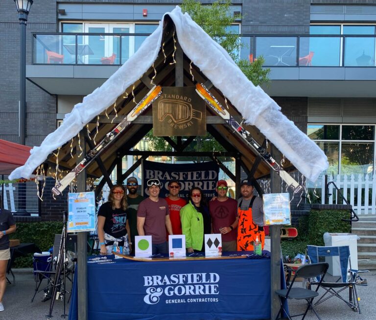 Group of people standing at a promotional booth with signage for Vondace Contracting, adorned with a mock snowy roof, at an outdoor event.