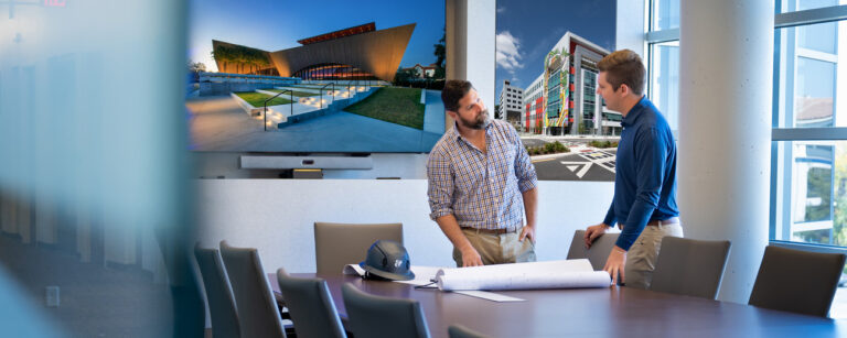 Two professionals discussing over a blueprint in a conference room with large window views of modern buildings in Orlando, Florida.