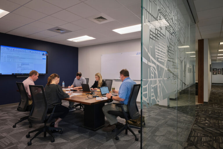 Team members engaged in a meeting with laptops around a conference table in a modern office setting, planning the best places to visit in Jackson.