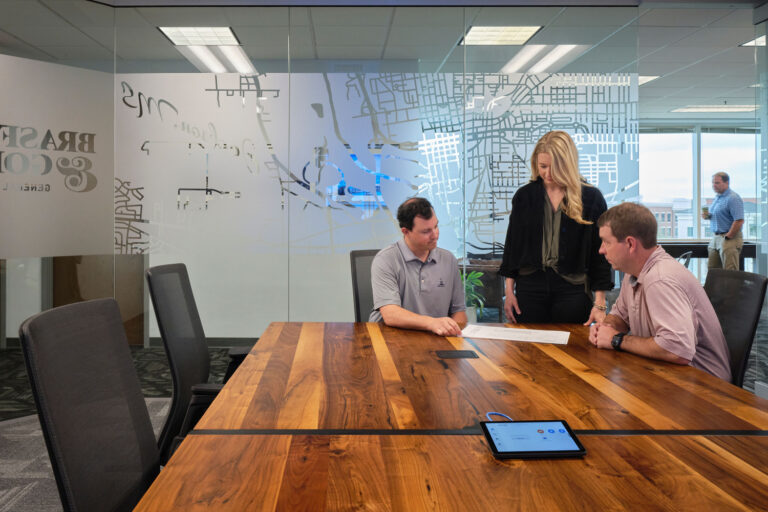 Three colleagues discussing a document in a modern office meeting room in Jackson, Mississippi.