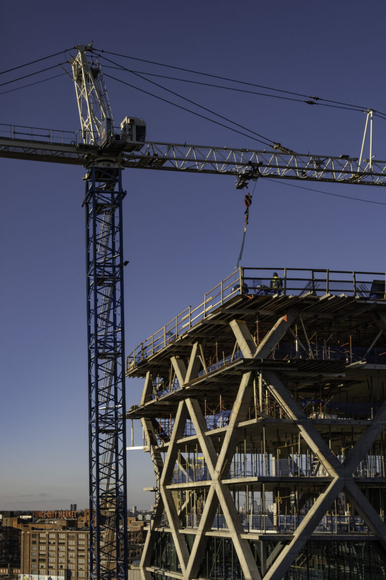 Construction crane towering over the framework of a building under construction against a clear blue sky,.