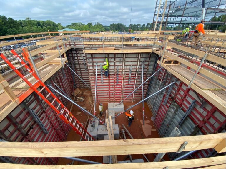 Ongoing construction in an area surrounded by wood, with an orange ladder allowing workers to descned into an enclosed space