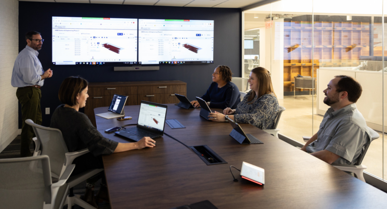 Professionals in a modern conference room in Birmingham, Alabama, engaged in a presentation with multiple screens displaying data.