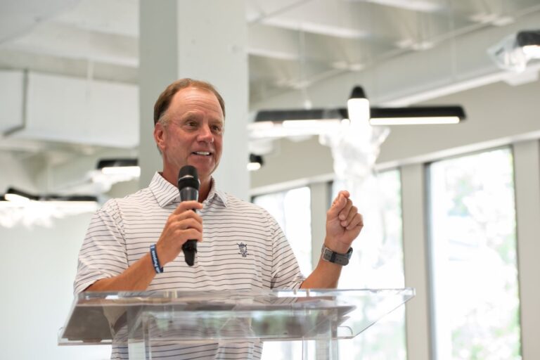 A man speaking into a microphone at a lectern in an illuminated room.