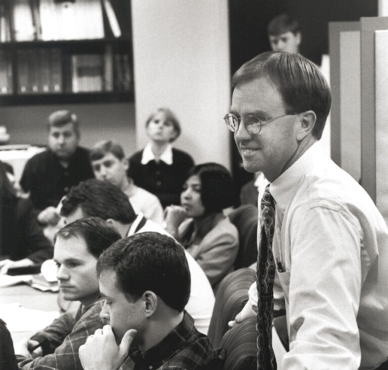Group of professionals in an office setting with a man in glasses smiling at the foreground.