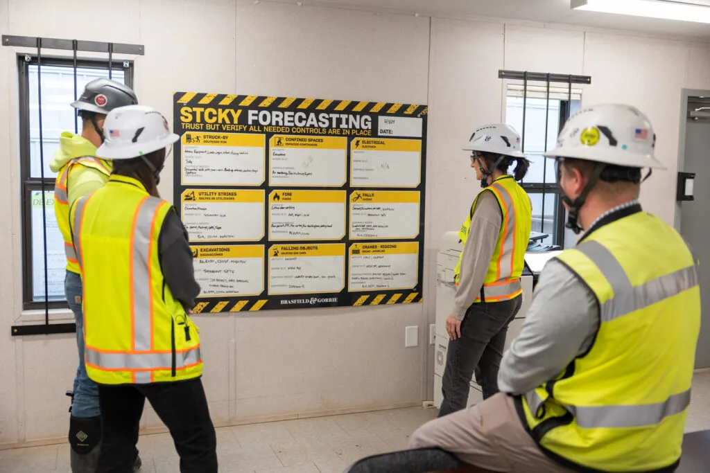 Construction workers gather around a safety board titled 